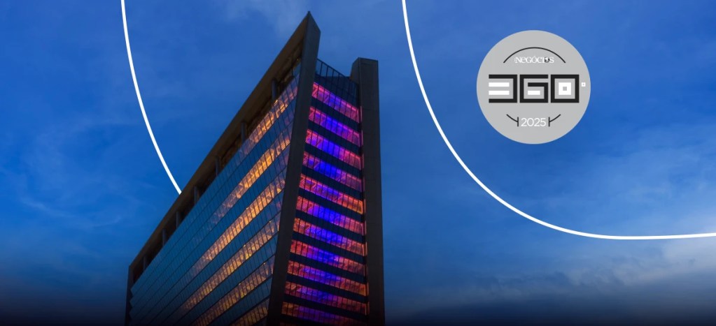 Edifício moderno iluminado com luzes coloridas na cidade durante o pôr do sol, destacando-se no cenário urbano.