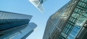 Imagem de arranha-céus de escritórios modernos em uma cidade, com uma perspectiva de baixo para cima, refletindo o céu azul claro e vidro.