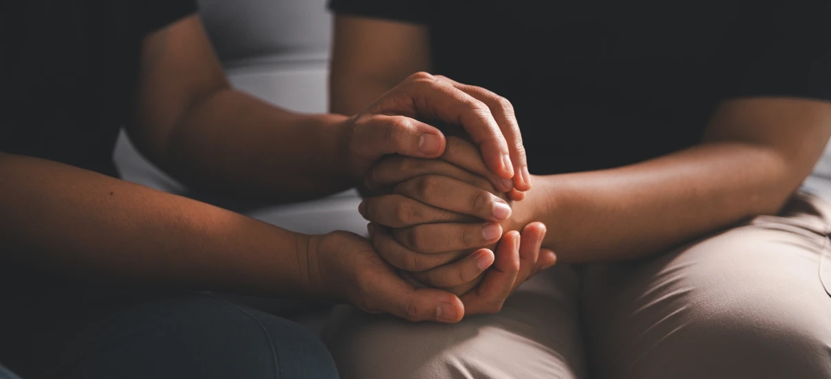 Imagem de duas pessoas segurando as mãos em sinal de apoio e solidariedade, demonstrando empatia e conforto em momento de dificuldade.
