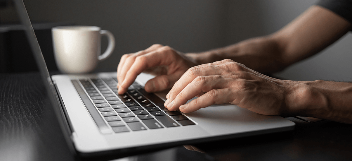 Pessoa usando um laptop em uma mesa de trabalho, focada na digitação, com uma xícara branca ao lado, ideal para negócios, trabalho remoto ou tecnologia.
