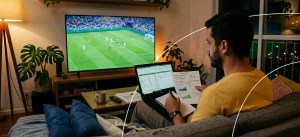 homem sentado assistindo jogo de futebol fazendo planejamento no computador e com papel